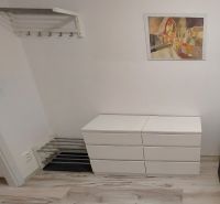 A studio apartment with a wood-patterned floor, white furniture, and a colorful painting on the wall.