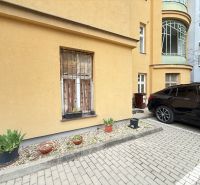 Parking in front of the building on Leškova Street in Bratislava with flower pots and a parked car.