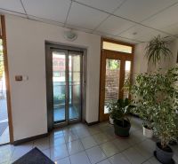 Office interior with tiled floor, elevator, and potted plants.