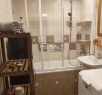 A bathroom in a 3-room apartment with a bathtub and shelves, complemented by a wooden rack.
