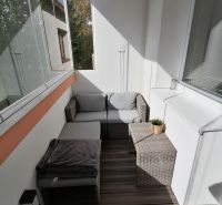 A glazed balcony with rattan furniture and a wooden decor floor in a studio apartment.