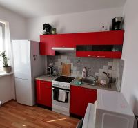 A kitchen with red cabinets and a wood-patterned floor in a studio apartment.