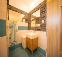 A bathroom in a family house with a sink, ceramic tiles, and wooden elements.