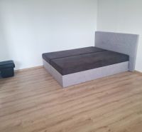A bedroom in a studio apartment with a bed and a wooden-patterned floor.