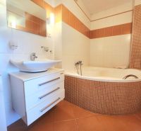 A bathroom with a corner bathtub, sink, and washing machine in a 3-room apartment.