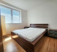 A bedroom with sunlight, a bed, a nightstand, and a wooden-patterned floor.