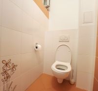 A toilet with white tiles and orange flooring in a 3-room apartment.