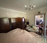 Bedroom in a family house with wardrobes and a table, bed with a decorative throw.