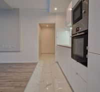 A kitchen with white cabinets and appliances in a 2-room apartment, flooring with a wood decor.