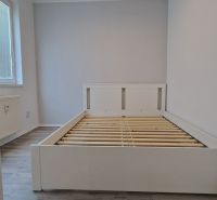 A double bed in a room with wood-patterned flooring and ceiling lighting.