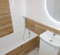 A bathroom with a bathtub and tiles with a wooden decor in a 2-room apartment.