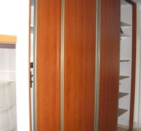 A built-in wardrobe with a wooden decor in a 2-room apartment, complemented by white walls and shelves.
