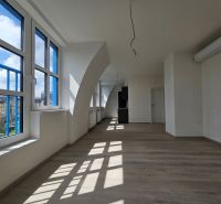 A spacious room with large windows, wooden decor flooring in a studio apartment.