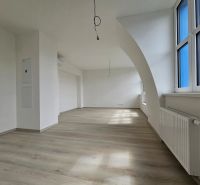 Spacious living room with wood-patterned flooring and large windows in a studio apartment.