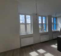 A bright room with three windows and a wooden decor floor in a studio apartment.