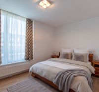 Bedroom with a large window, double bed, and wooden decor flooring in a 2-room apartment.