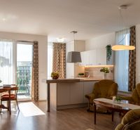 Living room in a two-room apartment with a wooden decor floor and a light kitchen.