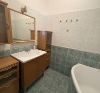 A bathroom in a 2-room apartment with a bathtub and a wooden cabinet.