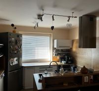 A kitchen in a family house with a metal range hood, floor with wooden decor.