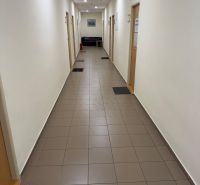 A narrow hallway in offices with tiles, doors, and a sofa at the end.