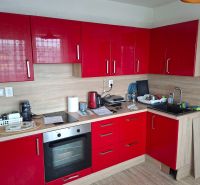 A kitchen in a 2-room apartment with red cabinets and a wooden decor floor.