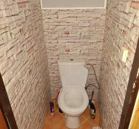 A bathroom with a toilet and walls with a brick wall decor in a 2-room apartment.
