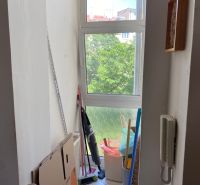 The window section of a 2-room apartment with cardboard boxes, cleaning supplies, and an intercom.