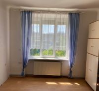 A room with a cabinet, a window, and curtains in a 2-room apartment, with a wooden decor floor.