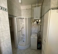 A bathroom with a corner shower and a washing machine in a 2-room apartment.