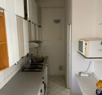 A narrow kitchen in a 2-room apartment with white furniture and tiles.