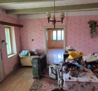 A room in a family house with older furniture, pink wallpaper, and wooden flooring.