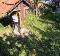 The garden of a family house in Dedinka with a lawn, a gas meter, and a pile of soil in the background.
