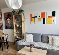 Living room in a two-room apartment with a sofa, table, and wooden decor flooring.