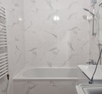 A bathroom in a 2-room apartment with a bathtub and a washing machine, tiled with light tiles.
