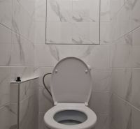A toilet with ceramic tiles in a 2-room apartment.