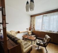 Living room in a three-room apartment with a wooden decor floor, retro furniture, and curtains.