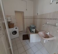 A bathroom in a 4-room apartment with a washing machine, bathtub, and sink on white tiles.