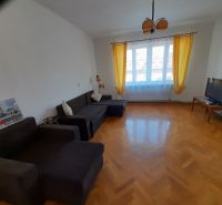 Living room with wood-patterned flooring, sofa, television, and yellow curtains.