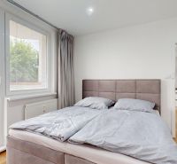 Bedroom in a studio apartment with large windows, a bed, and a wooden decor floor.