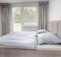 A bright bedroom with an upholstered bed and curtains in a studio apartment.