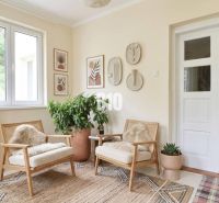 Interior of a family house with light-colored armchairs, greenery, and decorative paintings on the walls.