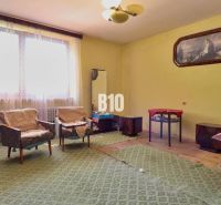 A room in a family house with armchairs, a table, and carpeted flooring.