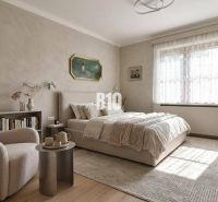 A bedroom in a family house with light walls, a bed, a chair, and decorations.