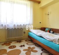 A room in a family house with a single bed, a wardrobe, and a window with white curtains.