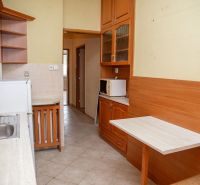 A kitchen with wooden cabinets, a sink, a microwave, and a dining counter in a two-room apartment.