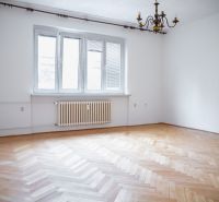 Empty room with a chandelier, white walls, and a wooden-patterned floor.