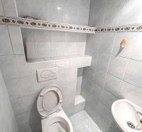 Bathroom with a toilet in a 2-room apartment, tiles with a simple pattern and a small sink.