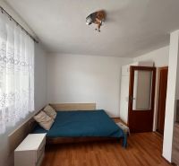 Studio apartment with curtains, bed, and wooden decor flooring.