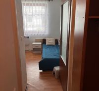 In the studio apartment, there is a blue bed, a nightstand, and a floor with a wooden decor.