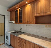 A kitchen in a 2-room apartment with a wooden decor kitchen unit and white tiles.